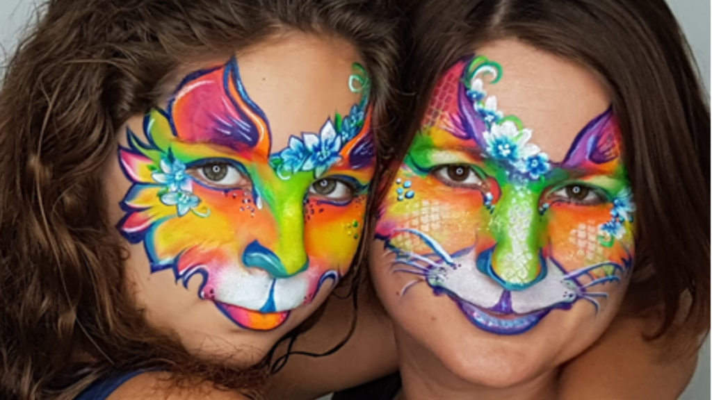 two women with painted faces of rainbow mercats